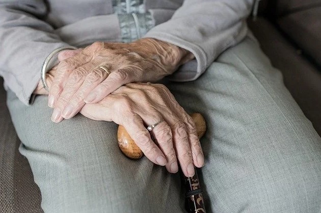 Senhora com mãos com rugas a segurar bengala à espera do cuidador de idosos.
