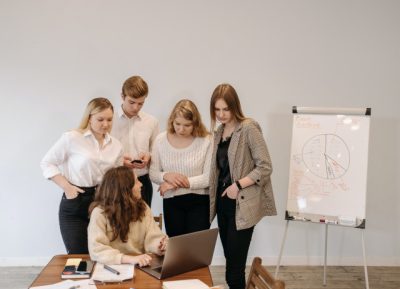 Jovens em volta de uma mesa e de mulher com computador num programa de trainee.